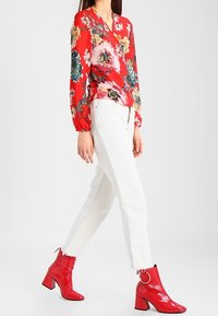 Blusa rossa a fiori con maniche lunghe abbinata a jeans bianchi a vita alta e stivaletti rossi lucidi con tacco a blocco e accenti circolari.