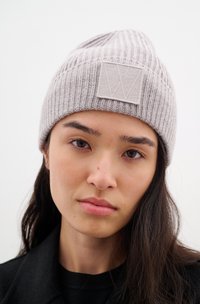 Šedý pletený beanie s žebrovanou strukturou a čtvercovou látkovou nášivkou s světlým šedým designem, těsný střih a měkký materiál.
