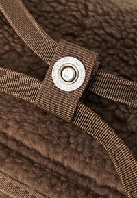Brown fleece material with a textured surface; features brown straps and a metallic button embossed with "THE NORTH FACE."