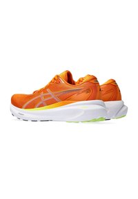 Des chaussures de course orange vif avec un haut en maille texturée, une semelle intermédiaire blanche et des accents verts sur la semelle extérieure. Détails réfléchissants présents.