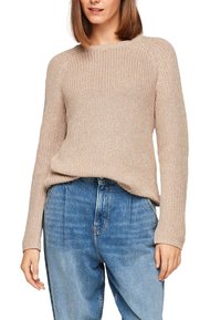 Beżowy sweter wykonany na drutach z okrągłym dekoltem i rękawami raglanowymi, połączony z wysokim stanem, lekko wyblakłymi niebieskimi dżinsami. Widoczna faktura tkaniny.