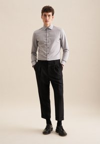 Grijze overhemd met verticale strepen, zwarte plooibroek en zwarte schoenen. De outfit heeft eenvoudige lijnen en een op maat gemaakte pasvorm.