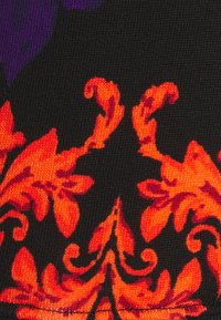 Tissu noir avec un motif floral orné en rouge et orange et des détails violets, montrant un gros plan de la texture tricotée du textile.