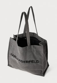 Grå stoff tote bag med to robuste håndtak, med svart brodert tekst "KARL LAGERFELD" og innvendig glidelåslomme for sikker lagring.