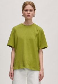 Grünes Baumwoll-T-Shirt mit lockerer Passform, kurzen �Ärmeln und rundem Ausschnitt. Der Stoff wirkt weich mit einer glatten Textur.