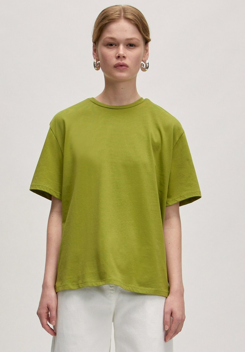 Grünes Baumwoll-T-Shirt mit lockerer Passform, kurzen Ärmeln und rundem Ausschnitt. Der Stoff wirkt weich mit einer glatten Textur.