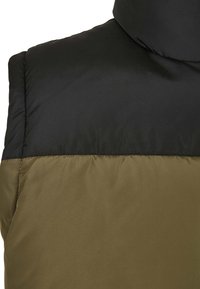 Vadderad väst med en svart övre del och en olivgrön nedre del, som visar en slät textur och en hög krage.