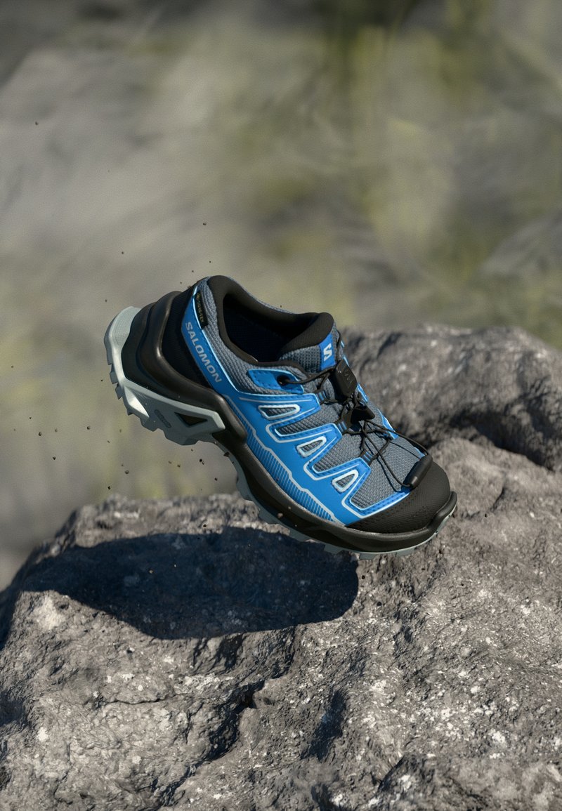 Melnas un zilas sporta kurpes ar teksturētu virsu, mīkstu apkakli un gumijas zoli, piedāvā ātras stiprināšanas sistēmu un izteiktu zoles rakstu.