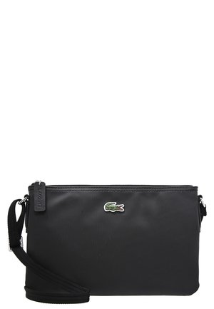 Czarna torba Lacoste typu crossbody z teksturowaną powierzchnią, małym zielonym logo krokodyla, regulowanym paskiem oraz zamkiem błyskawicznym na górze.