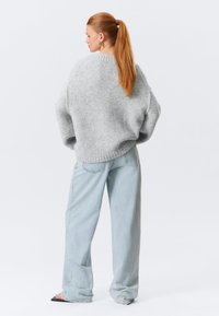 Pull gris clair oversize en tissu texturé, ourlet côtelé et épaules tombantes, associé à un jean à jambes larges bleu clair.