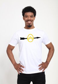 Bílý bavlněný tričko s grafickým vzorem černé šipky a žlutého štítu uprostřed. Jednobarevné, s kulatým výstřihem a krátkými rukávy.