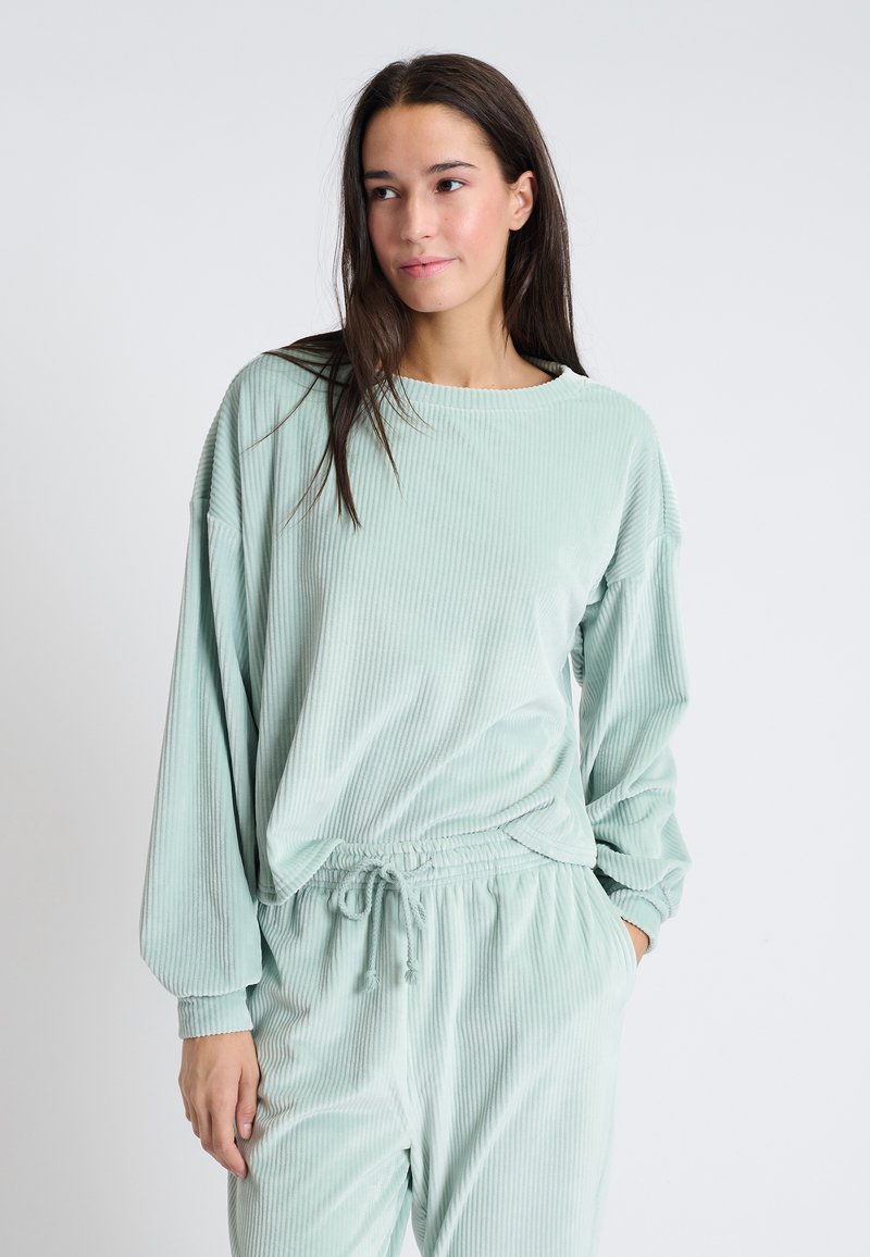 Ensemble de détente vert clair en tissu doux et côtelé. Comprend un haut à coupe décontractée avec un col rond et un pantalon à cordelette assorti.