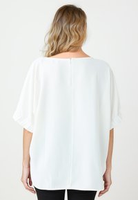 Witte blouse met een losse pasvorm, brede bootnek, korte puffmouwen en een rits aan de achterkant. Glad, lichtgewicht materiaal.