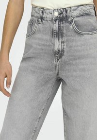 Jeans de mezclilla gris con cintura alta y corte holgado. Cuenta con bolsillos frontales, cierre de botón y una textura desgastada con variaciones sutiles.