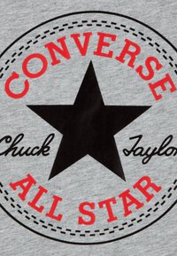 Tela gris con un logo circular que tiene una estrella negra. El texto en rojo y negro dice "CONVERSE", "Chuck Taylor" y "ALL STAR".