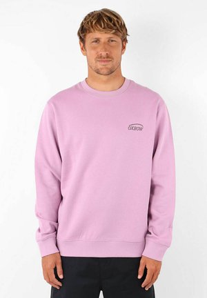 Sweatshirt rose clair à manches longues, avec des poignets côtelés et un col rond ; présente un petit logo brodé sur la poitrine. Texture lisse.