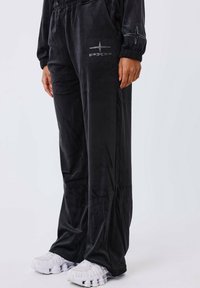 Zwarte fluwelen joggers met een losse pasvorm, voorzien van zijzakken en een sterontwerp in zilveren versiering op de linker bovenbeen.