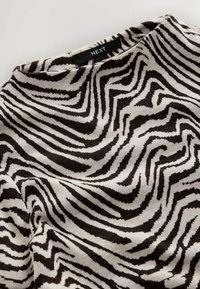 Pletený top s čiernobielym vlnitým zebrovým vzorom, širokým výstrihom a jemnou textúrou, s označením "NEXT" na golieri.