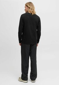 Schwarzes Langarmshirt, kombiniert mit gestreiften schwarzen Hosen. Das Outfit zeichnet sich durch eine lockere Passform und lässige Sneaker aus.
