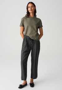 T-shirt en coton vert olive à manches retroussées associé à un pantalon noir à motifs avec cordon de serrage et des chaussures plates noires. Design simple et décontracté.