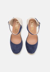 Talons espadrilles en daim marine avec des accents en tissu tissé. Dotées d'un bout arrondi et d'une sangle à boucle pour un ajustement sécurisé.