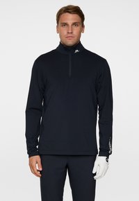 Maglietta nera a maniche lunghe con colletto alto e zip a quarti. Presenta un logo sul colletto e sulla manica. Tessuto liscio e leggero.