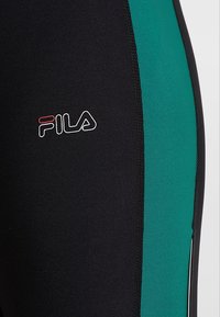 Czarne legginsy z zielonym bocznym panelem, wykonane z elastycznego materiału. Posiadają logo Fila w białym i czerwonym kolorze na lewym udzie.