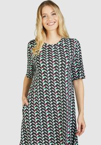 Schwarzes Kleid mit kurzen Ärmeln, das ein geometrisches Muster in Pink, Weiß und Grün aufweist. Hat seitliche Taschen und einen lässigen Schnitt.
