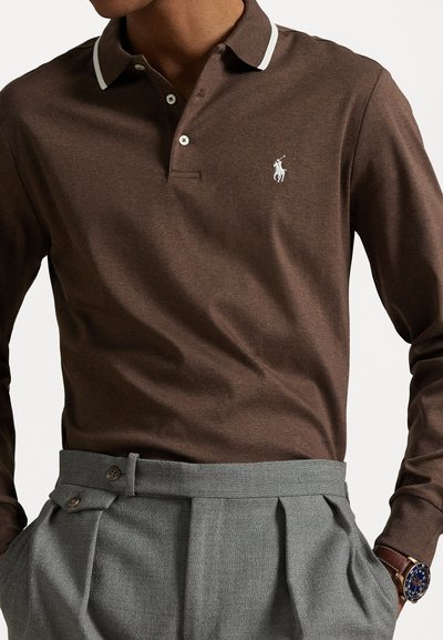 Bruine lange mouwen polo met witte kraagaccenten en geborduurd logo, gecombineerd met hooggesneden grijze broek met plooien.
