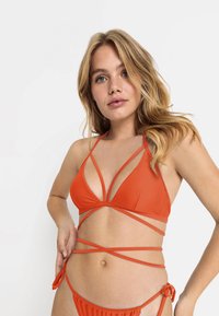 Oranje bikini met een driehoekige top met kruisende banden, en een broekje versierd met verstelbare knopen aan de zijkanten. Soepele textuur.