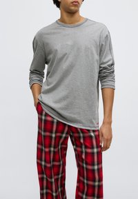 Gray long-sleeve shirt made of cotton, paired with red plaid pajama pants featuring black and white stripes. Slim fit with rolled sleeves.