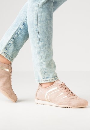 Lichtblauwe jeans zichtbaar vanaf halverwege het onderbeen naar beneden, gedragen met lichtroze vetersneakers met witte strepen aan de zijkanten, staand op een witte ondergrond.