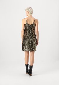 Vestido mini de lantejoulas preto e dourado com alças finas, apresentando um design ajustado e textura brilhante. Combinado com botas de salto alto pretas.