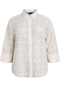 Koronkowa bluzka w kremowym kolorze z zapięciem na guziki z przodu, kołnierzykiem i rękawami o długości trzech czwarte. Posiada skomplikowane wzory kwiatowe i teksturowany materiał.