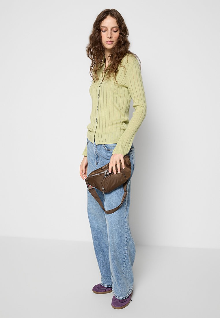 Hellgrüner gerippter Cardigan, blaue weit geschnittene Jeans und lila Schuhe. Braune Umhängetasche mit Reißverschlussdetails und verstellbarem Tragegurt.