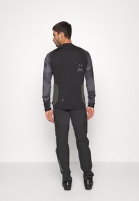 Chemise noire à manches longues avec des accents gris et un logo. Associée à un pantalon gris foncé avec des poches et un marquage sur le côté.