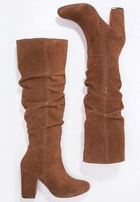 Bottes en nubuck marron au-dessus du genou avec un design décontracté, un talon bloc haut, un bout rond et un subtil détail de fermeture éclair latérale.