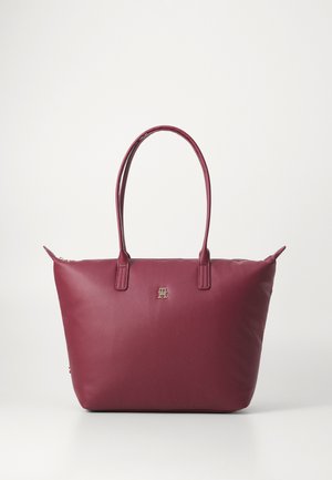 Sac fourre-tout bordeaux en matériau synthétique lisse, avec des doubles poignées, un accent logo doré à l'avant et une fermeture zippée sur le dessus.