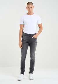 Sive ozke jeans hlače iz denima, s klasičnim dizajnom petih žepov. Nosijo se s enostavno belo majico in belimi športnimi copati.