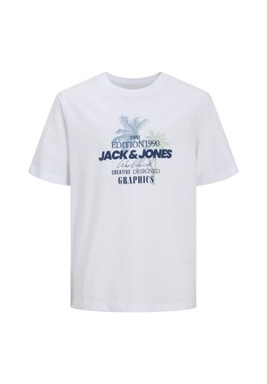 Garçon souriant portant une casquette bleue, un t-shirt blanc imprimé, un short gris foncé mi-cuisses, des chaussettes blanches et des baskets blanches, debout sur un fond uni.