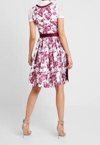 Bloemjurk met een fitted lijfje en een uitlopende rok, voorzien van een witte achtergrond, roze bloemenpatronen, kantmouwen en een bordeauxrode riem.