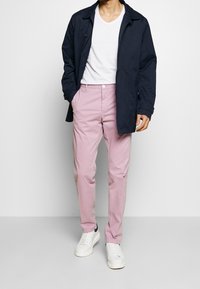 Marineblå yderjakke, hvid V-hals t-shirt og lyserøde bukser med lige snit. Hvide sneakers med marineblå detaljer fuldender looket.