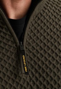 Olijfgroene gebreide pullover met een geprofileerd diamanten patroon, voorzien van een zwarte rits en een label met de tekst "PME LEGEND" in het geel.
