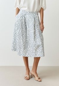 Polven mittainen vaaleansininen hame, jossa on valkoinen abstrakti kuvio. Siinä on istuva vyötärö ja sivutaskut. Yhdistetty beigeihin korollisiin mules-kenkiin.