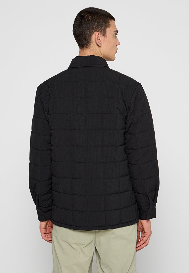 Svart vadderad jacka med långa ärmar, krage och knäppte manschetter. Har en texturerad tyg och rak skärning vid fållen.