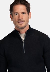 Schwarzer ribbeliger Pullover mit einem Viertelreißverschluss-Kragen. Glatte Textur, figurbetontes Design und eine kontrastierende innere Schicht. Einfach und funktional.