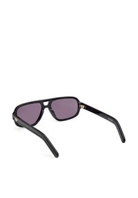 Czarne plastikowe okulary przeciwsłoneczne z fioletowymi soczewkami. Posiadają kwadratową ramkę, proste zauszniki oraz złoty akcent z boku. Gładka tekstura na całej powierzchni.