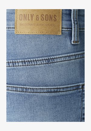 Light blue denim jeans with contrasting brown stitching. Features a tan leather label with "ONLY & SONS" and "PASSIONATE JEANS MAKERS" text.
