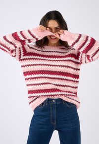 Maglione a righe in tonalità di rosa con maniche ampie e texture a costine. Abbinato a jeans in denim scuro a vita alta.