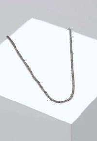 Collana a catena intrecciata in argento con una texture liscia, caratterizzata da un design classico e un leggero luccichio, poggiata su una superficie bianca di esposizione.